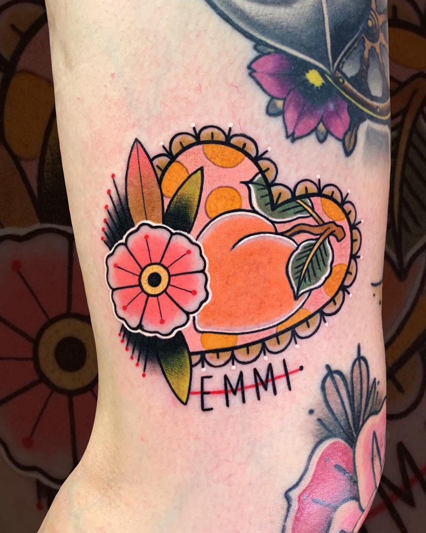 Bold, traditional-style tattoo of a peach with flowers and leaves, personalized with the name "Emmi"